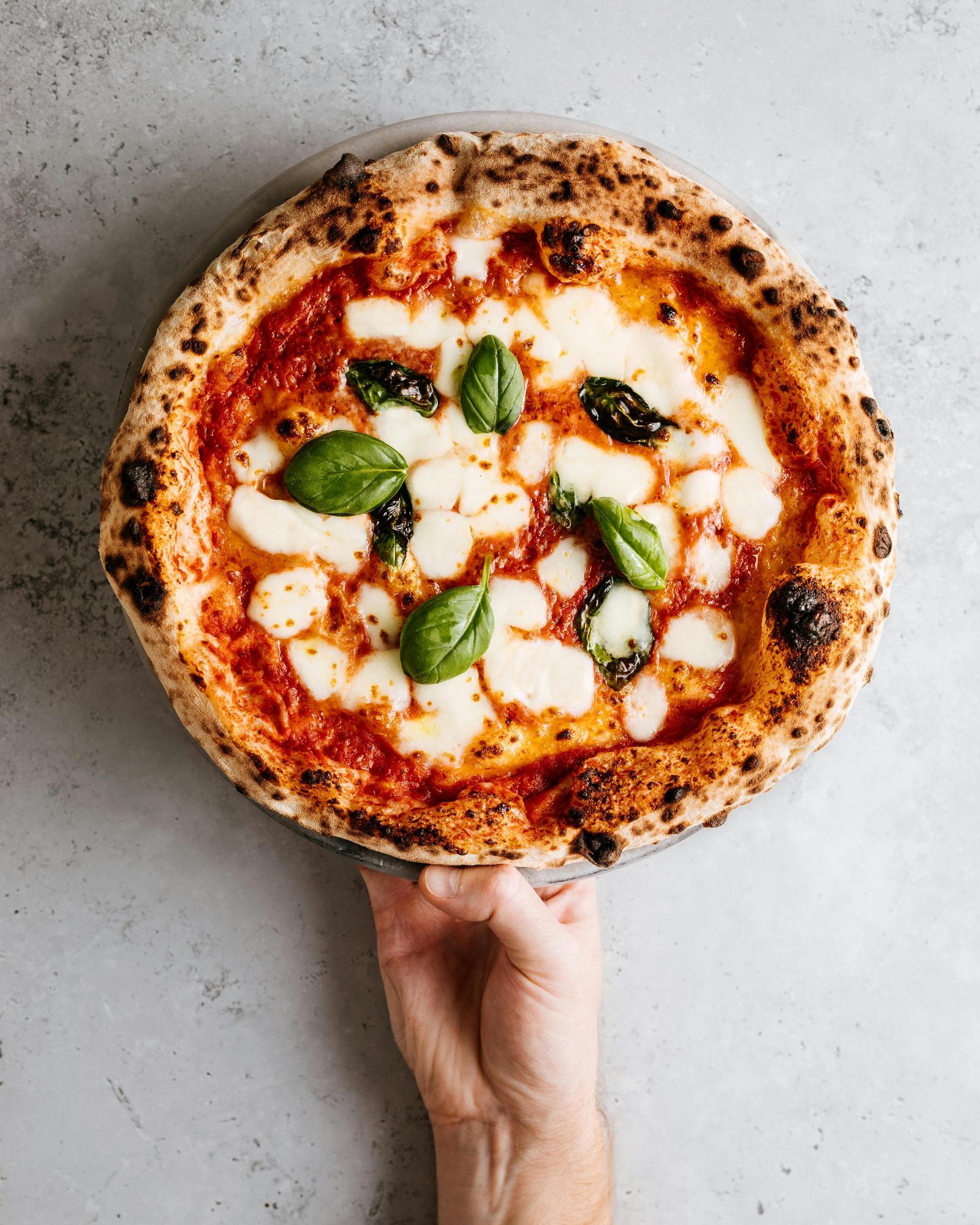 Mano sosteniendo una pizza margarita